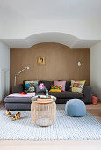 Graues Polstersofa mit bunten Kissen vor brauner Wand und Couchtisch im Wohnzimmer