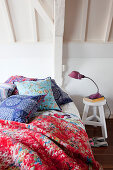 Colourful scatter cushions and quilt on bed in white attic room
