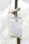 Lantern decorated with white lace hangs on the garden pavilion made of branches and a curtain