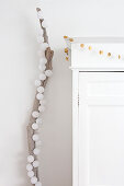 Christmas decorations on white cupboard next to cotton ball fairy lights on branch