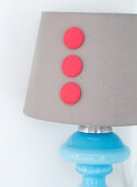 Three red, fabric-covered buttons on the lampshade of a table lamp