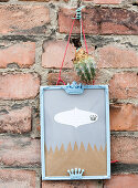 Picture frame with crowns and cactus hanging from a brick wall