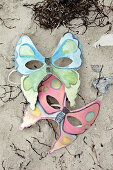 Selbstgemachte Masken mit Schmetterling-Motiv im Sand