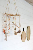Mobile made of shells and driftwood in front of a white plank wall