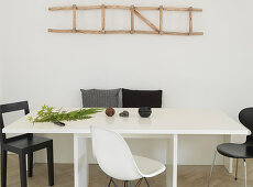 Wooden ladder as a decoration on the wall above the dining table with black and white chairs