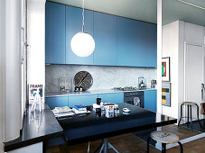 Black dining table in a modern open kitchen with blue fronts