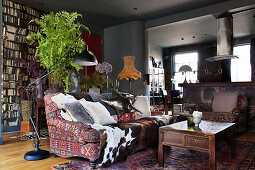 Cushions and animal fur on a sofa with ethnic cover, behind a console table with a houseplant in the living room