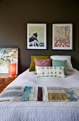 Scatter cushions and fabric samples on bed below pictures on dark wall in bedroom