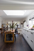 Dining table and open-plan kitchen in long room with skylight