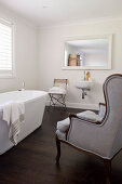 Antique armchair in bathroom with free-standing bathtub and wooden floor