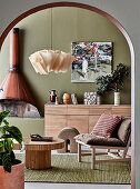 Blick durch Rundbogen auf Designer-Rattantisch, Stuhl, Sideboard und Kamin im Wohnzimmer mit olivgrüner Wand