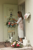 Frau ordnet Utensilien an Haustüre mit Ordnungshelfer, Korb mit Rosenblüten