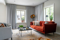 Red sofa in living room with pale grey curtains