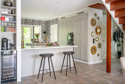 Kitchen counter with barstools and collection of mirrors on wall in open-plan interior