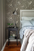 Double bed with headboard and bedside table in bedroom with brown wallpaper