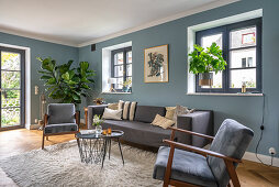 Grey sofa set, coffee table and houseplants in living room with blue wall