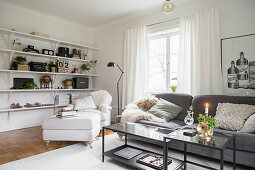 White armchair and ottoman in front of shelves and grey sofa