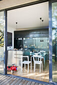Blick von Holzterrasse durch geöffenete Terrassentür in Küchenbereich mit Stahlinsel und Esstisch