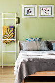 Metal ladder used as rack next to wooden bed against pastel green wall