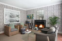 Rattan and upholstered armchairs grouped around open fireplace in living room with grey wallpaper