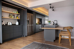 Charcoal-grey kitchen cabinets running through two rooms with chairs at small island counter