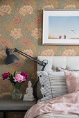 Vase of peonies next to bed against floral art nouveau wallpaper