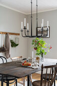 Old table with wooden top and chairs below cast iron candle chandelier in dining area
