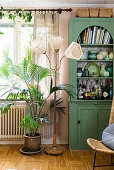 Collection of ceramics in green, glass-fronted cabinet, standard lamp and potted palm in living room