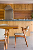 Esstisch mit Polsterstühlen vor Küche mit Holzschränken und Holzrückwand