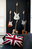 Union-flag cushion on sofa in front of guitars on black wall