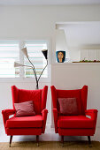 Two red armchairs with scatter cushions in front of white wall