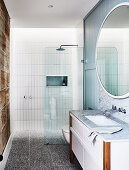 Runder Spiegel über Waschtisch mit Marmorplatte im Badezimmer mit Duschbereich