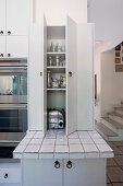 White kitchen cupboard with open doors over tiled worksurface in country-house kitchen