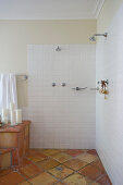 White-tiled open shower area in bathroom with terracotta floor tiles