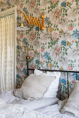 Extendable wall lamp above metal bed in bedroom with floral wallpaper
