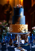 Tiered cake in dark blue and gold on glass cake stand