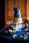 Tiered cake and flowers on table festively set in dark blue
