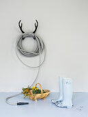 Garden hose coiled on antler-shaped, wall-mounted rack, basket and wellington boots