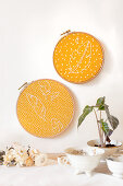 Feathers embroidered on yellow patterned fabric in embroidery frames decorating wall