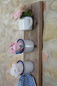 Organiser made from enamel mugs on wooden board leaning against rustic stone wall