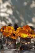 Posies of pot marigolds in beakers wrapped in felt and twine