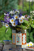 Bouquet of wildflowers with ox-eye daisies, meadow sage, honesty flowers and blackberry sprig in tea caddy