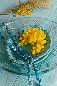 Turquoise necklace and mimosa flowers on ceramic dish