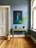 Green console table below picture of peacock on blue wall in period building