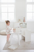 Kleines Mädchen am Spieltisch im Kinderzimmer ganz in Weiß