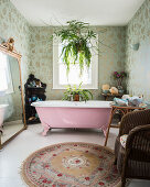 Free-standing pink bathtub in cosy bathroom with patterned wallpaper