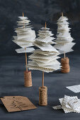 Miniature fir trees made from skewered book pages on cork bases against black background