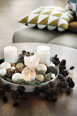 White candles and Christmas baubles on plate in wreath of pine cones