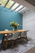 Shell chairs at wooden table next to blue wall and on patterned floor tiles