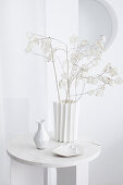 Deco in white: silver leaf branches in a zigzag vase on side table